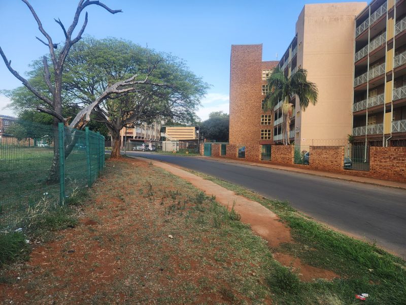 Street view of a multi-story apartment complex featuring brick exterior walls, balconies, and perimeter security fencing.