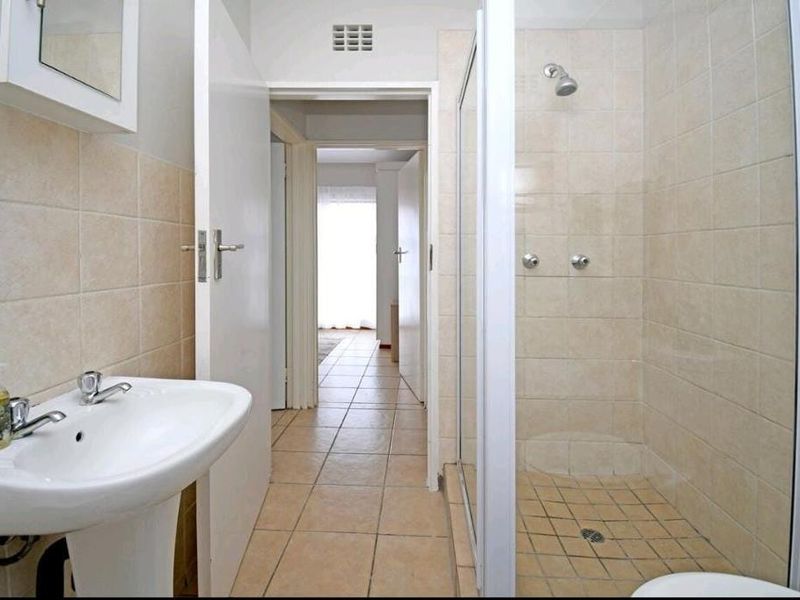 A functional bathroom featuring a pedestal basin, a tiled shower enclosure, and neutral wall and floor tiling.