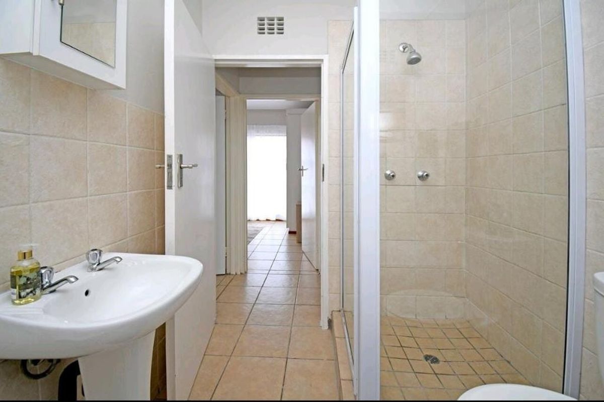A functional bathroom featuring a pedestal basin, a tiled shower enclosure, and neutral wall and floor tiling.