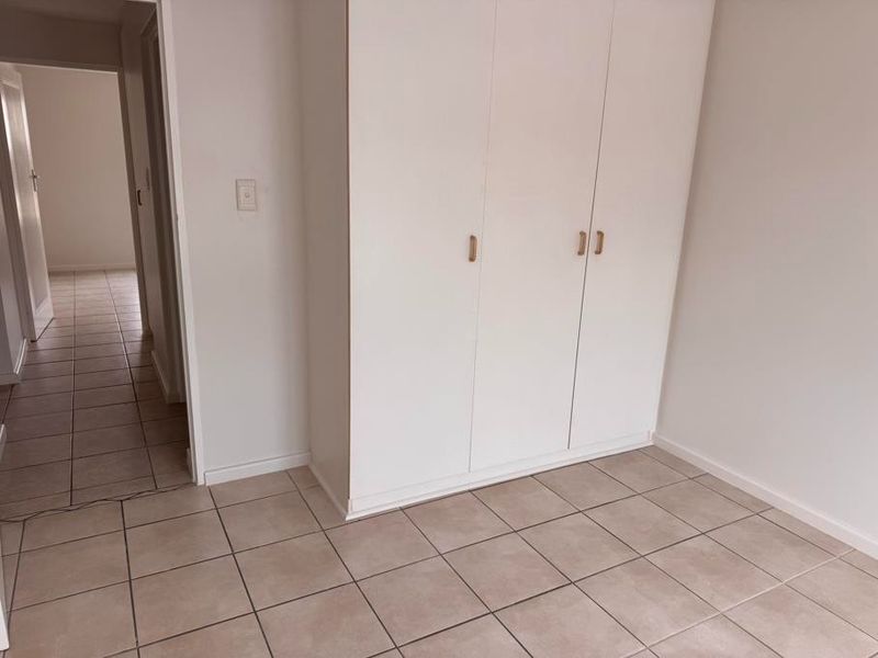 A clean, empty bedroom featuring neutral tiled flooring and white built-in cupboards, offering a blank canvas for personalization.