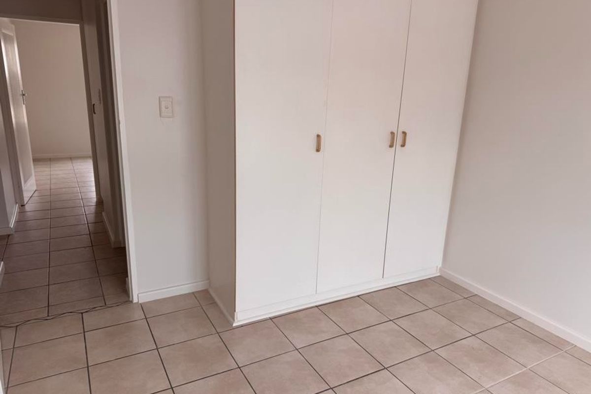 A clean, empty bedroom featuring neutral tiled flooring and white built-in cupboards, offering a blank canvas for personalization.