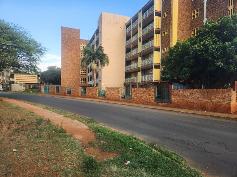 Street view of a multi-story apartment complex featuring brick facade, balcony access, and a secure perimeter wall.