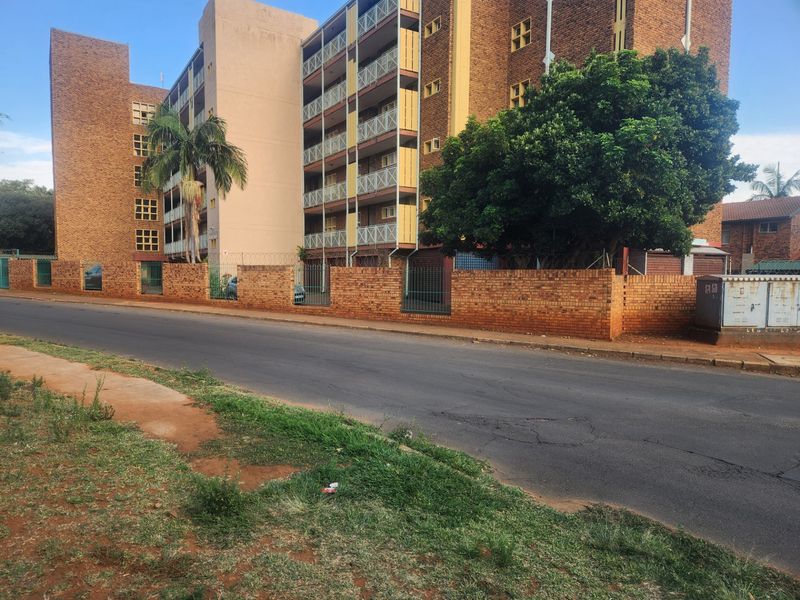 Street view of a multi-story brick apartment complex featuring balconies and a perimeter brick boundary wall with security fencing.