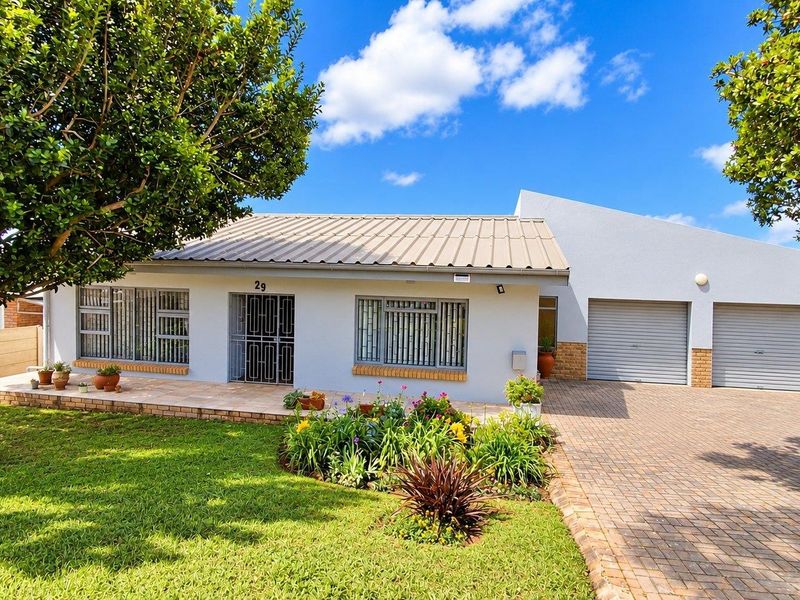 Front view of a well-maintained single-story house featuring a paved driveway, double garage, and a neat front garden with a paved patio area.