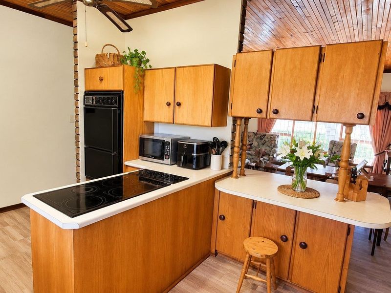 A functional kitchen featuring timber cabinetry, built-in oven, electric cooktop, and a breakfast bar, with a warm timber-paneled ceiling overhead.