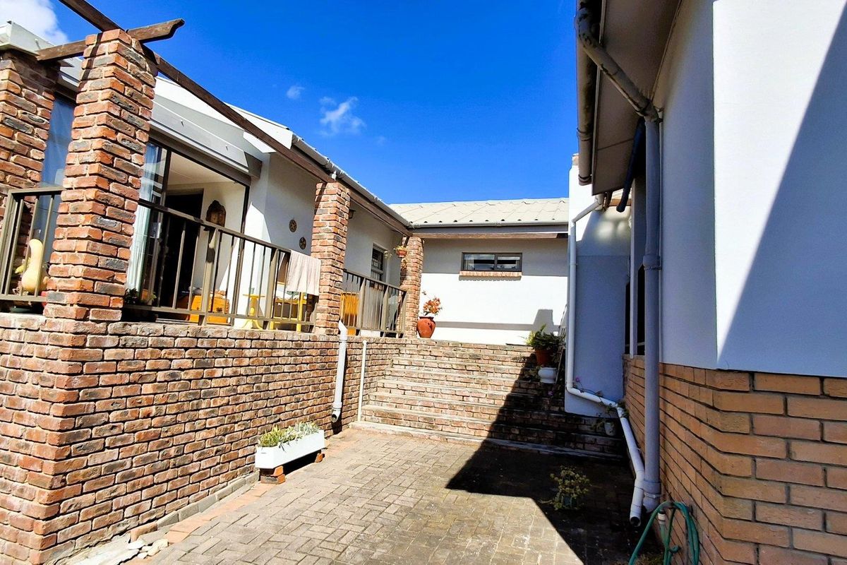 A rear courtyard area featuring brick paving, a raised brick retaining wall, and a timber pergola structure connecting the building sections.