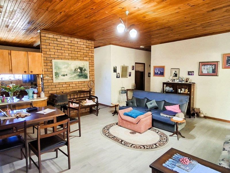 Open plan living and dining area featuring a timber ceiling, exposed brick wall, and light-toned laminate flooring, seamlessly connected to the kitchen space.