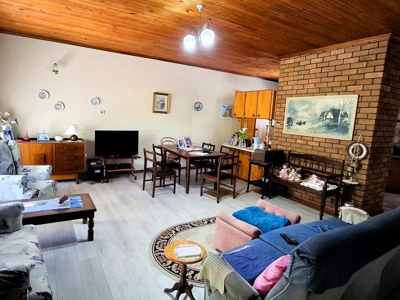 Spacious open-plan living and dining area featuring a prominent brick fireplace, exposed timber ceiling, and modern laminate flooring.
