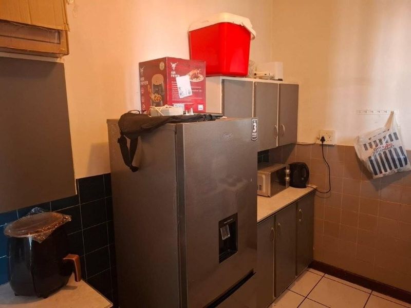 A compact kitchen area featuring built-in cabinetry, tiled backsplash, and tiled flooring, currently showing signs of wear and dated finishes.
