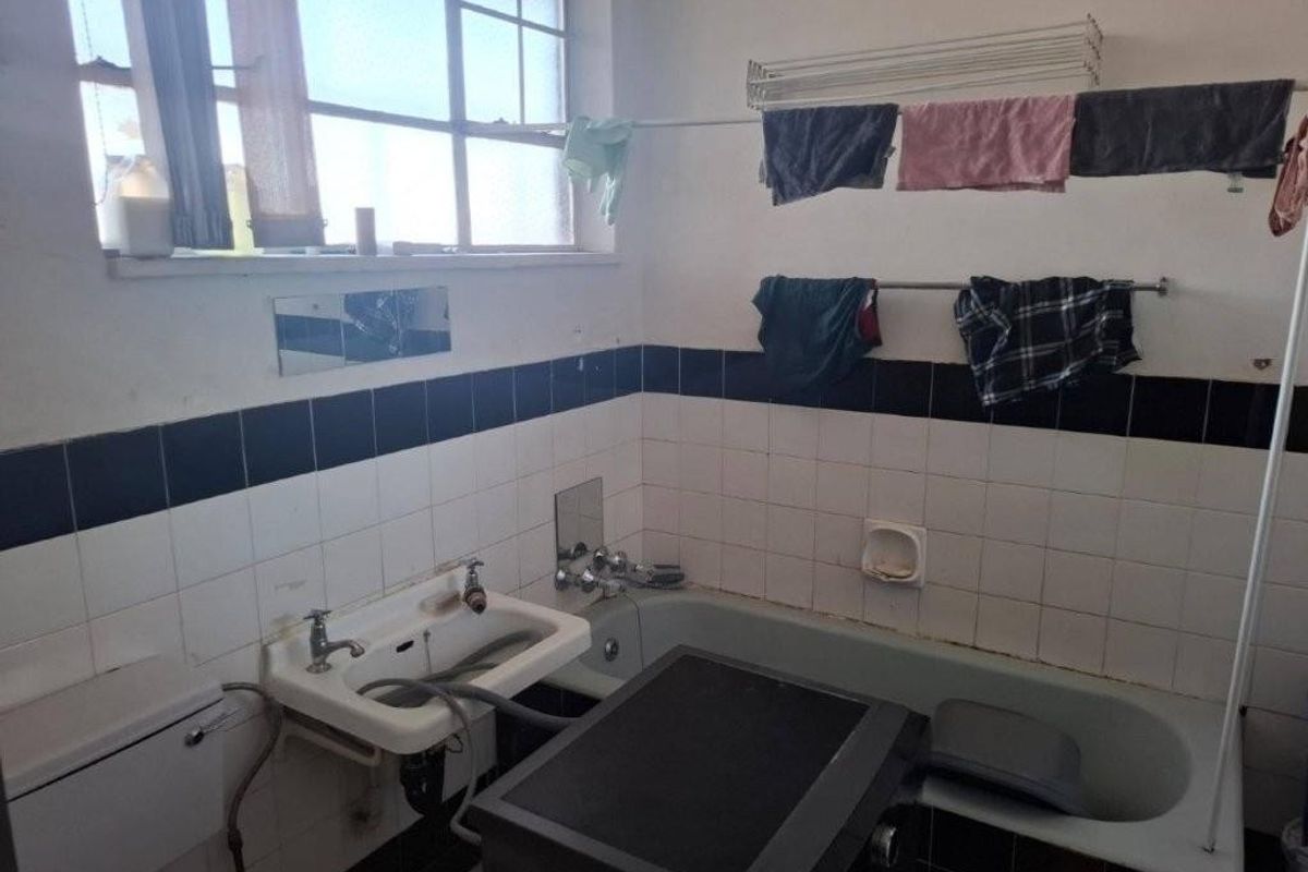 A functional bathroom featuring a bathtub and wall-mounted basin with tiled splashbacks, requiring cosmetic updates to improve its overall condition and aesthetic appeal.