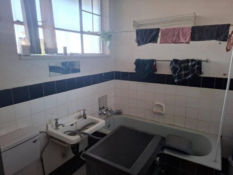 A functional bathroom featuring a bathtub and wall-mounted basin with tiled splashbacks, requiring cosmetic updates to improve its overall condition and aesthetic appeal.