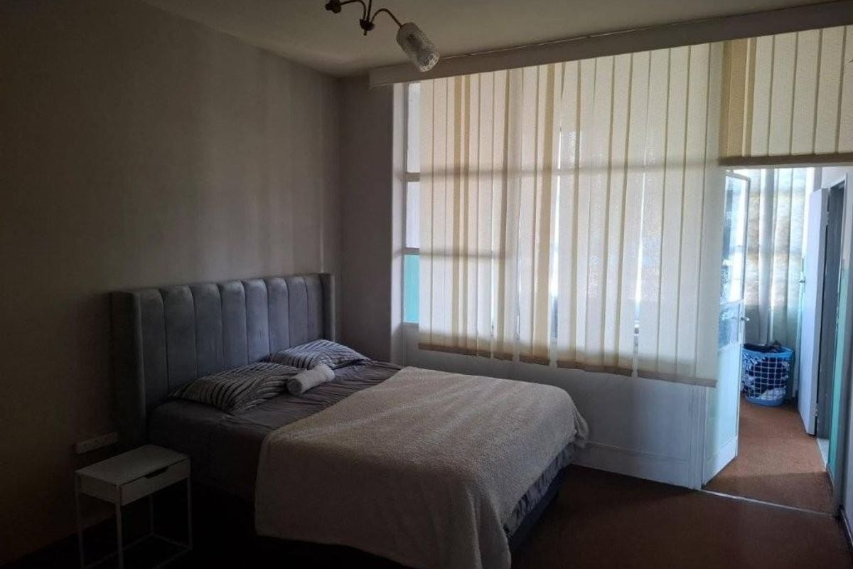 A bedroom featuring large windows with vertical blinds and a ceiling light fixture, offering a functional space with natural light.