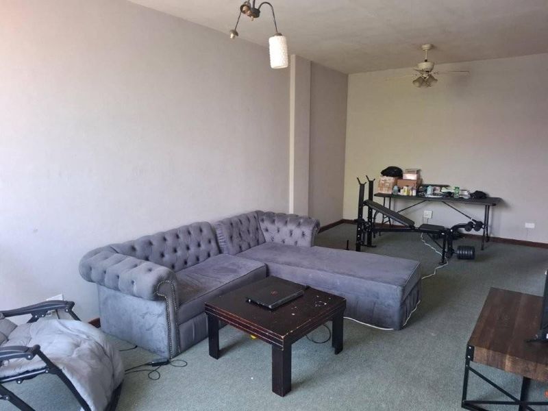 A living room area featuring carpet flooring, a ceiling fan, and a pendant light fixture, currently used as a multi-purpose living and exercise space.