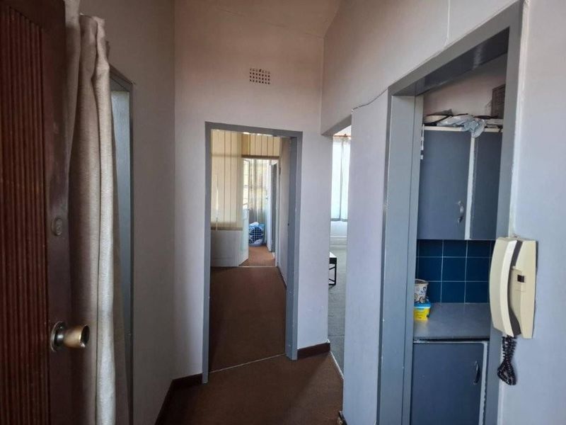 A functional apartment hallway connecting multiple rooms, featuring built-in cabinetry and an intercom system, requiring cosmetic updates to flooring and paintwork.