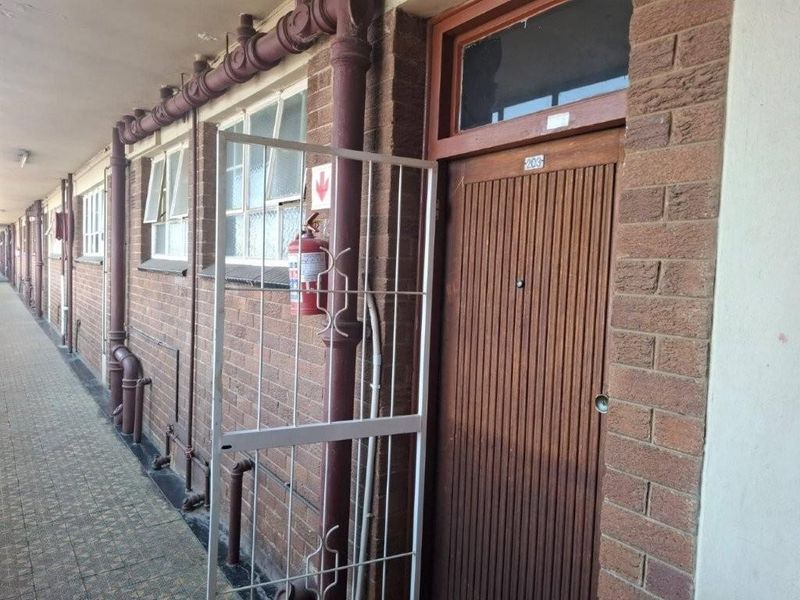 Exterior apartment hallway featuring brick facade, security gate, and exposed plumbing infrastructure.