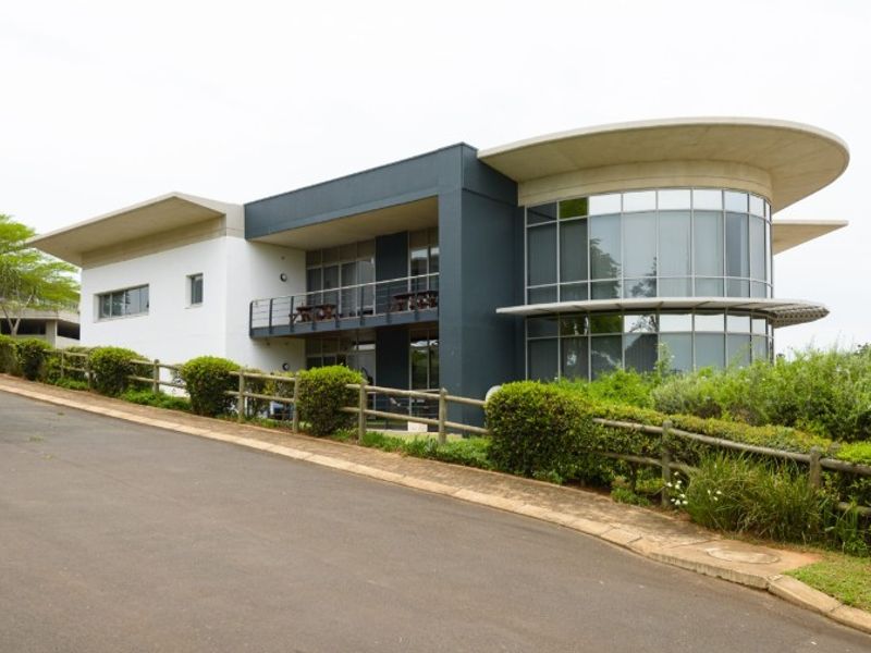 Modern office building featuring a striking curved glass facade, cantilevered roof design, and a private balcony overlooking the landscaped grounds.