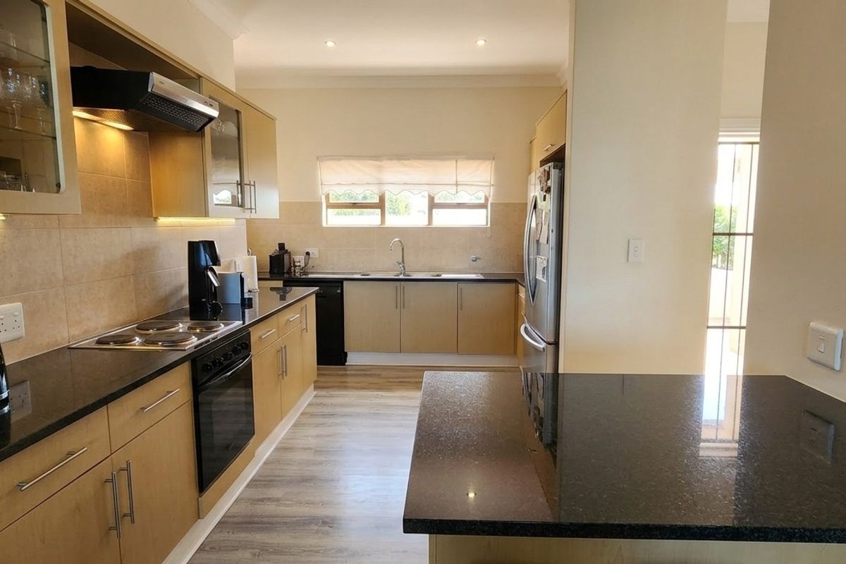 A well-maintained kitchen featuring granite countertops, built-in oven, electric hob, extractor fan, and ample cabinetry with under-cabinet lighting.