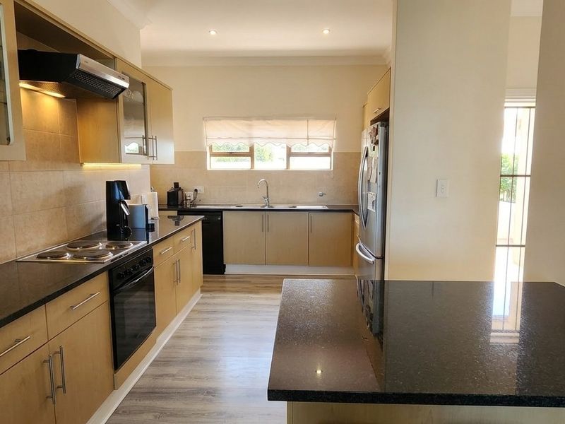 A well-maintained kitchen featuring granite countertops, built-in oven, electric hob, extractor fan, and ample cabinetry with under-cabinet lighting.