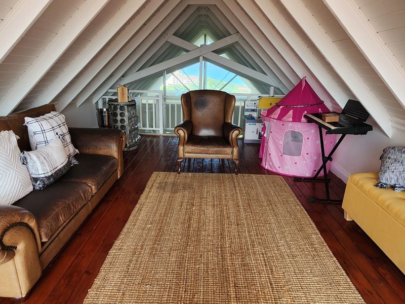 Attic-style living room featuring exposed timber rafters, warm timber flooring, and direct access to a balcony area.