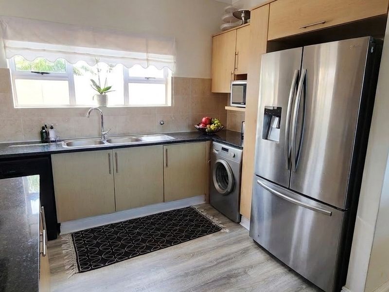 A functional kitchen featuring light wood cabinetry, granite countertops, a double basin sink, and integrated appliance spaces with a modern laminate floor finish.