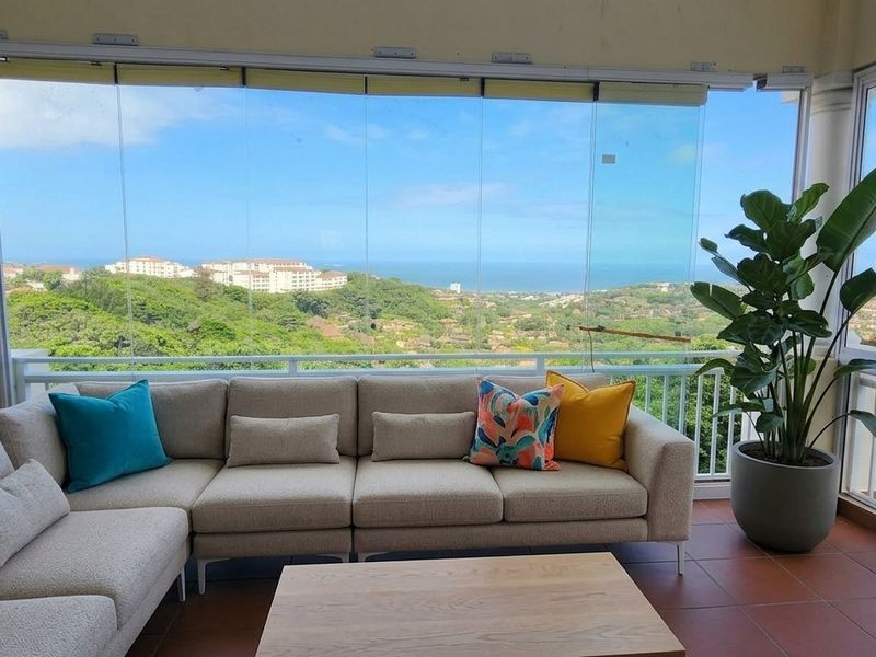 Enclosed balcony featuring glass panels, tiled flooring, and panoramic coastal views, providing a versatile outdoor living space.