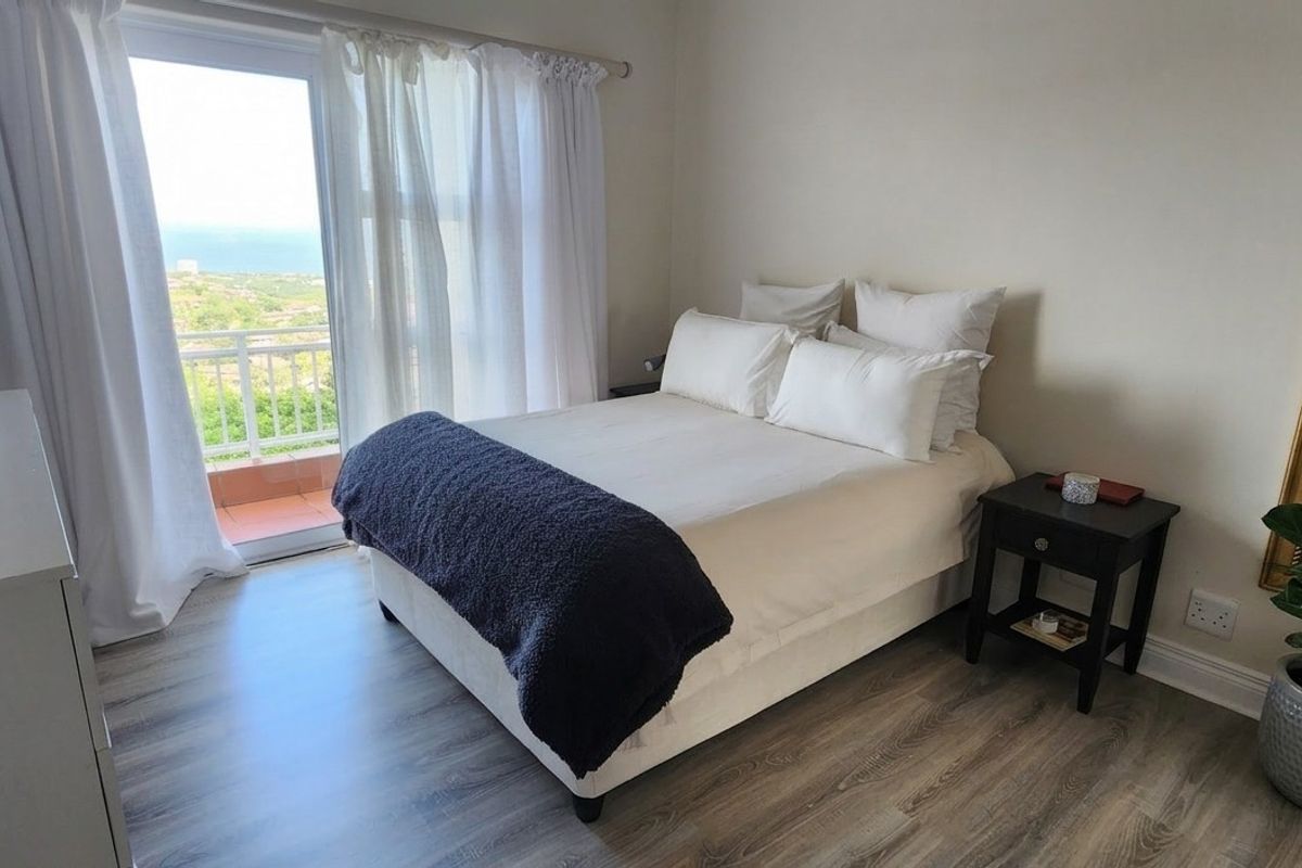 A bright bedroom featuring modern laminate flooring and a sliding glass door that opens onto a balcony with scenic views.