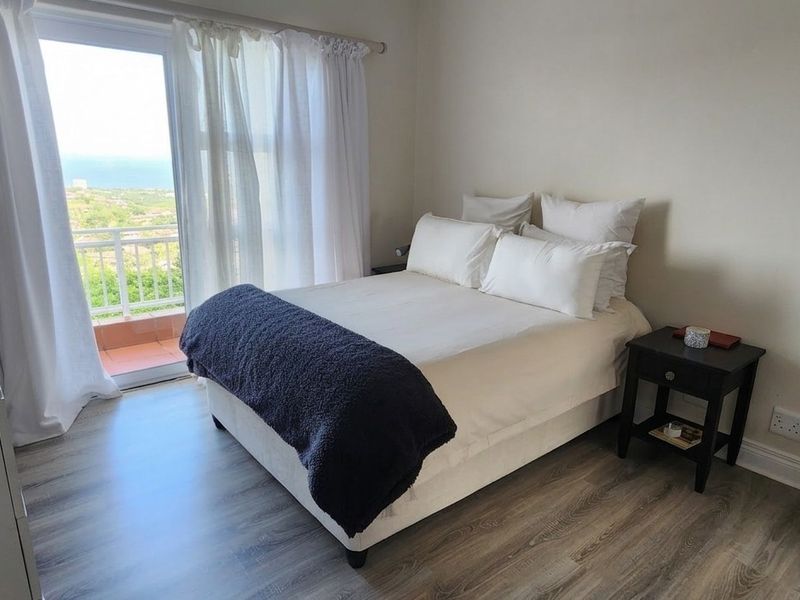 A bright bedroom featuring modern laminate flooring and a sliding glass door that opens onto a balcony with scenic views.