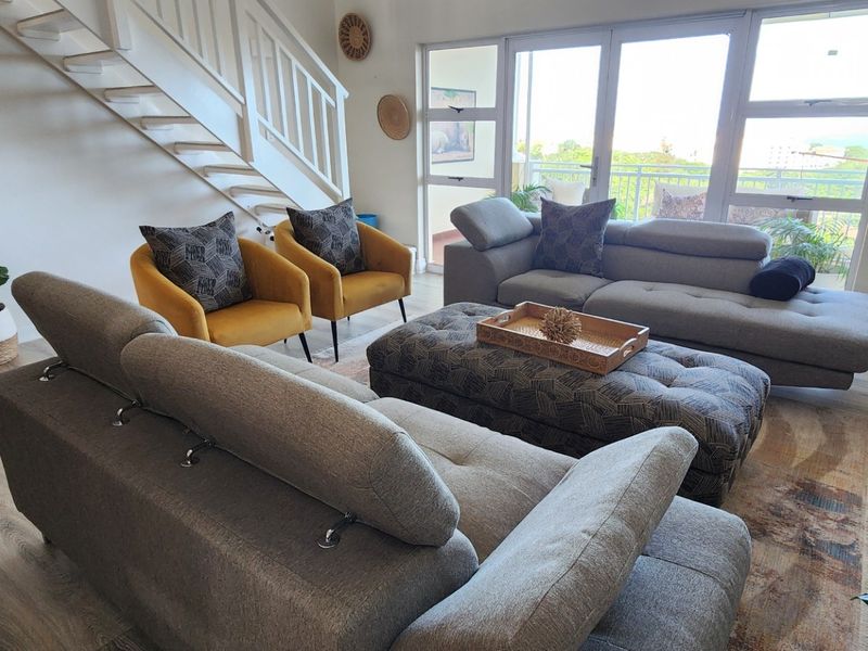 A bright and spacious living room featuring modern laminate flooring, a staircase, and large glass doors providing access to a balcony.