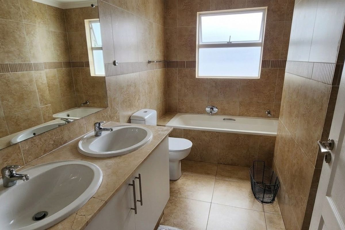 A well-maintained bathroom featuring a double vanity with built-in cabinetry, a bathtub, and neutral floor-to-ceiling wall tiles.