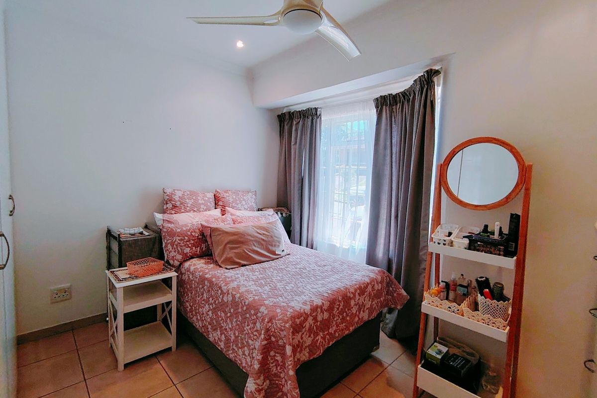 A compact bedroom featuring tiled flooring, a ceiling fan, and large windows with curtain tracks, providing a functional and well-lit living space.