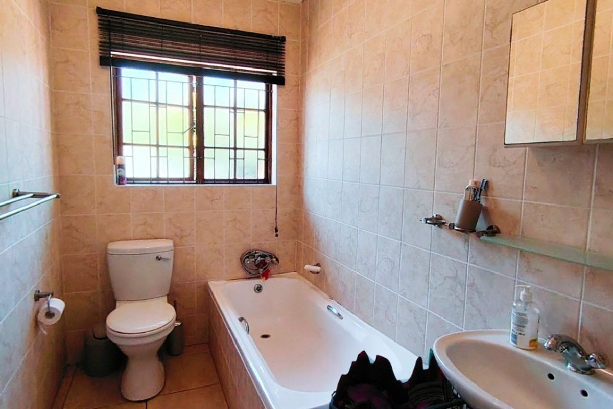 A functional bathroom featuring a bathtub, pedestal basin, and toilet, finished with neutral wall and floor tiles.