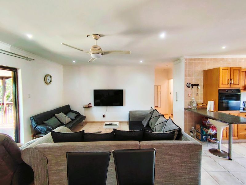 Open-plan living area featuring tiled floors, recessed lighting, a ceiling fan, and a functional kitchen with built-in oven and breakfast bar.