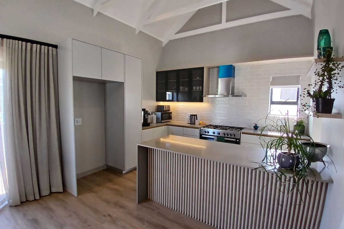 Modern kitchen featuring a slatted island, stone countertops, subway tile backsplash, gas hob, and high vaulted ceilings with exposed beams.