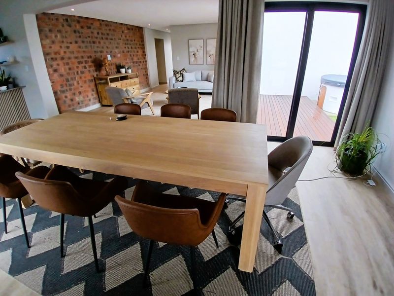 Spacious open-plan living and dining area featuring an exposed brick wall, modern laminate flooring, and large sliding doors leading to an outdoor deck.