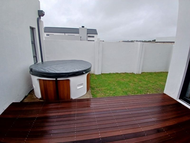 A private outdoor patio area featuring timber decking, a built-in hot tub, and a landscaped garden enclosed by a solid boundary wall.