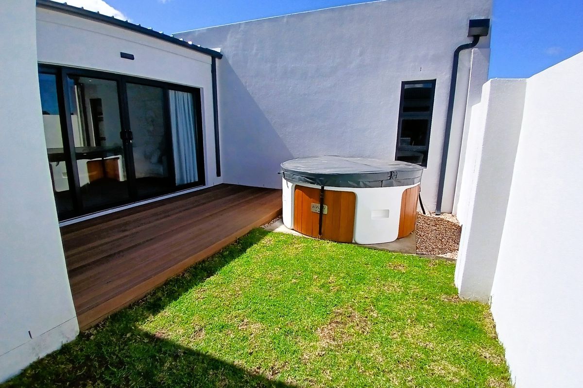 A private rear courtyard featuring timber decking, a built-in hot tub, and a small lawn area, accessible via sliding glass doors.