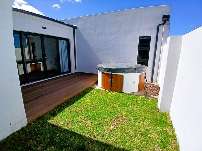 A private rear courtyard featuring timber decking, a built-in hot tub, and a small lawn area, accessible via sliding glass doors.
