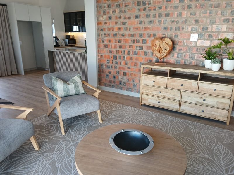 An open-plan living area featuring a striking exposed brick wall, modern kitchen cabinetry, and light laminate flooring, creating a warm and contemporary atmosphere.