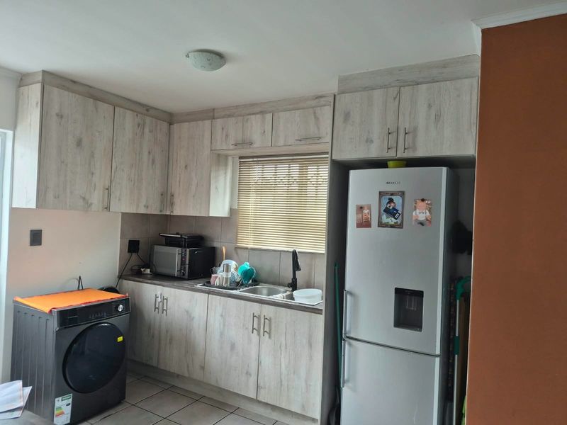 A functional kitchen featuring light wood-grain cabinetry, tiled backsplash, and integrated space for appliances, offering a practical layout for daily use.