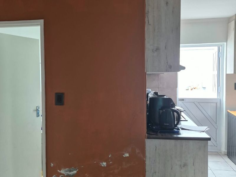 Kitchen area featuring built-in cabinetry and tiled flooring, showing visible signs of wall surface deterioration and peeling paint requiring maintenance.