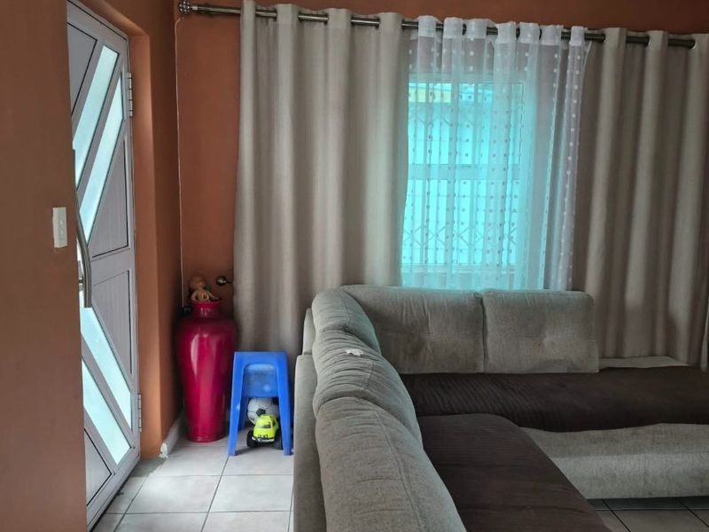 A living room area featuring tiled flooring, a security door, and a window fitted with security bars.
