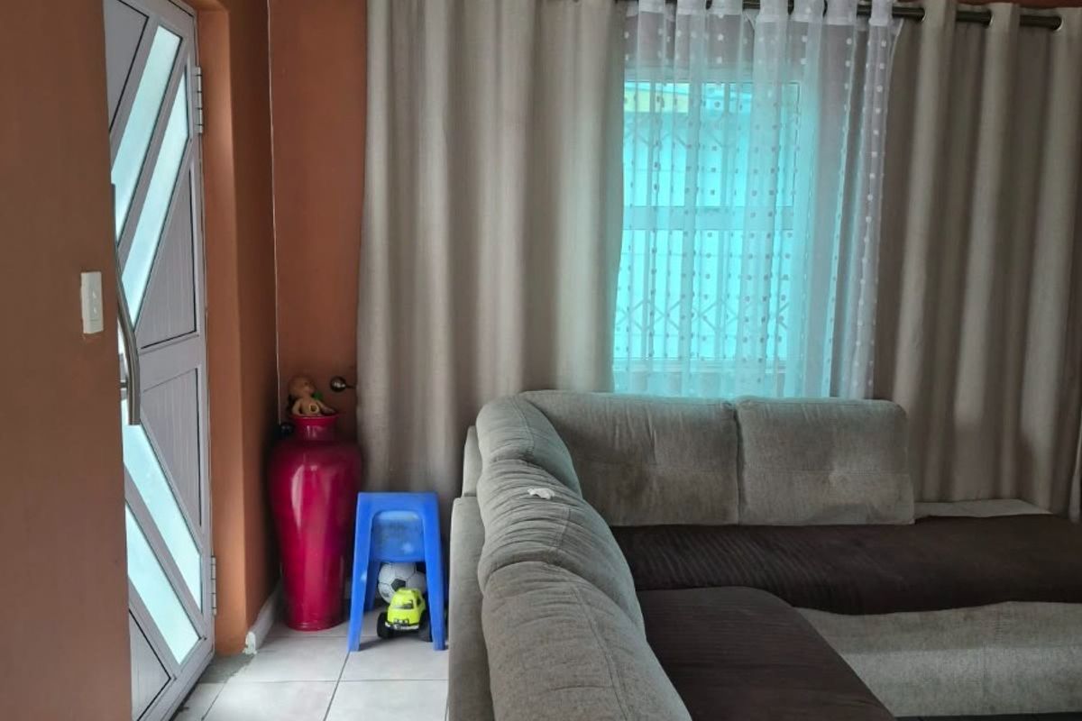 A living room area featuring tiled flooring, a security door, and a window fitted with security bars.