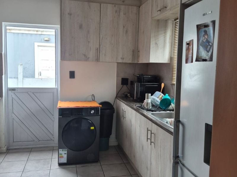 A functional kitchen featuring light wood-grain cabinetry, tiled flooring, and direct access to the exterior through a side door.