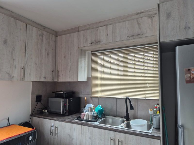 A functional kitchen featuring light wood-look laminate cabinetry, a double bowl stainless steel sink with a modern black mixer tap, and tiled backsplash.