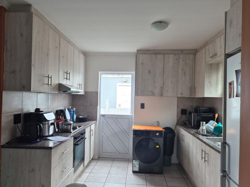 A functional kitchen featuring light wood-grain cabinetry, tiled flooring, built-in oven, extractor fan, and a rear access door.