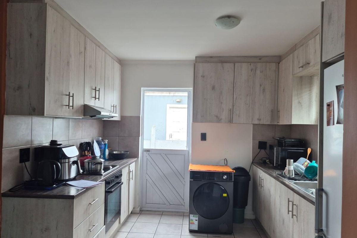 A functional kitchen featuring light wood-grain cabinetry, tiled flooring, built-in oven, extractor fan, and a rear access door.