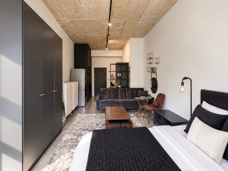 Modern open-plan studio apartment featuring an exposed concrete ceiling, sleek built-in wardrobe, and contemporary tiled flooring in a well-maintained space.