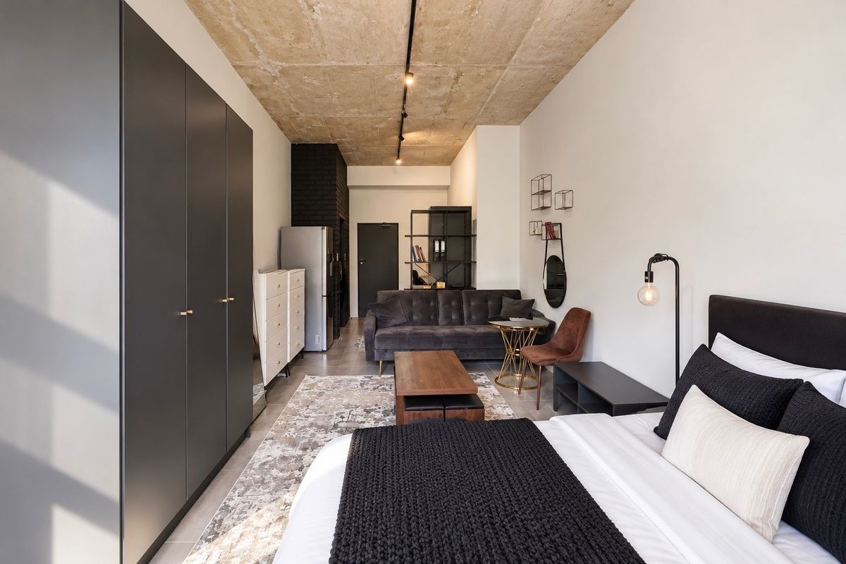 Modern open-plan studio apartment featuring an exposed concrete ceiling, sleek built-in wardrobe, and contemporary tiled flooring in a well-maintained space.