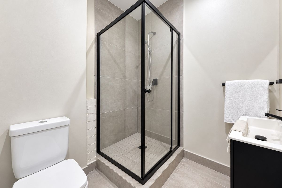 Modern bathroom featuring a sleek glass shower enclosure with black framing, a contemporary vanity, and neutral floor-to-ceiling tiling.