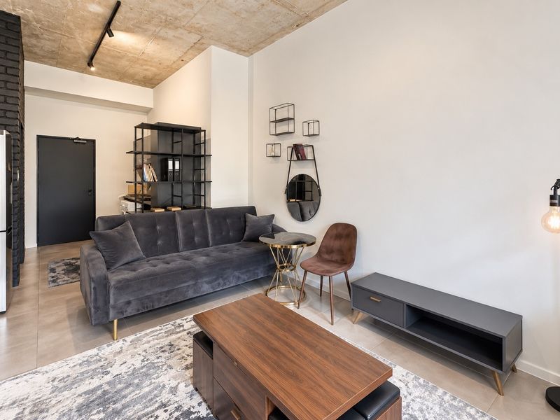 Modern living room featuring an exposed concrete ceiling, sleek tiled flooring, and a striking black brick accent wall, creating a contemporary industrial aesthetic.